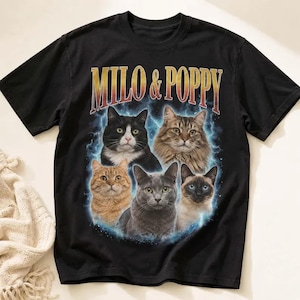 May include: A black short-sleeve t-shirt featuring the text MILO & POPPY in a yellow and orange gradient font above a graphic of five cats arranged in a circle against a blue lightning background, including a tuxedo, tabby, orange, grey, and Siamese cat.