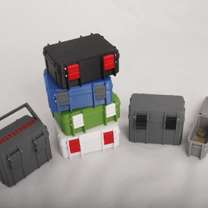 Könnte beinhalten: Eine Sammlung kleiner, farbenfroher Kunststoff-Aufbewahrungsboxen. Die Boxen sind in verschiedenen Farben erhältlich, darunter Schwarz, Blau, Grün und Weiß, mit roten und grauen Akzenten. Auf einer Box steht das Wort "BRIDGETTIER".