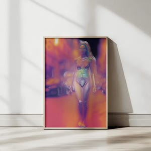 Puede incluir: Una impresión artística enmarcada que presenta una imagen borrosa y abstracta de una persona en traje de baño. La obra de arte tiene una paleta de colores rosa, naranja, morado y azul. La impresión se muestra en una pared blanca con suelo de madera.