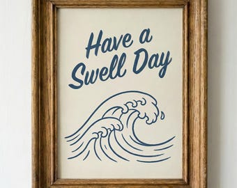 May include: A framed print with the words "Have a Swell Day" in dark blue script above a stylized wave illustration. The print is in a wooden frame and hangs against a white paneled wall.