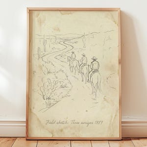 May include: A framed pencil sketch titled "Field sketch: Three amigos 1887." The artwork depicts three figures on horseback riding along a desert path, with cacti and a winding road in the background. The sketch has a vintage, aged appearance.