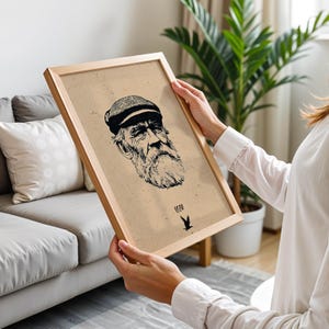 May include: A framed print featuring a detailed black and white illustration of an elderly man with a long beard and a cap. The print has a light brown background and a wooden frame. The text "1880" and a bird graphic are at the bottom.
