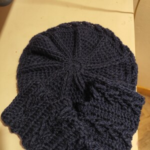 Peut inclure: Un bonnet bleu marine tricoté avec une écharpe assortie. Le bonnet est rond avec un motif texturé, et l'écharpe est attachée. La matière tricotée semble douce et chaude, adaptée au temps froid.