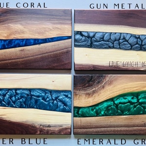 May include: Four wooden cutting boards with a river of epoxy resin in different colors. The colors are blue coral, gun metal grey, glacier blue, and emerald green. The boards are all made of walnut wood and have a natural finish. The boards are all approximately 12 inches long and 6 inches wide.