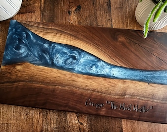 May include: A large wooden serving board with a blue and white epoxy resin inlay. The board is engraved with the text "Greggo "The Meat Master""