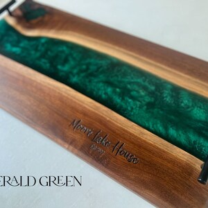 May include: A wooden serving tray with a green epoxy resin inlay. The tray has black metal handles and is engraved with the text "Moore Lake House Est. 2022" and "EMERALD GREEN".