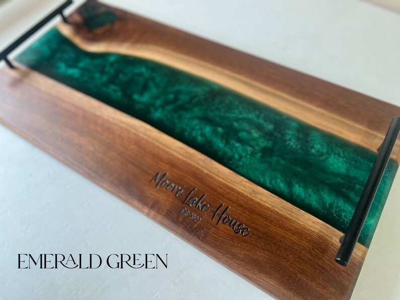 May include: A wooden serving tray with a green epoxy resin inlay. The tray has black metal handles and is engraved with the text "Moore Lake House Est. 2022" and "EMERALD GREEN".