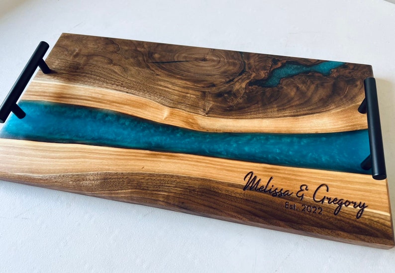 May include: A wooden serving tray with a blue resin inlay and black metal handles. The tray is engraved with "Melissa & Gregory Est. 2022".