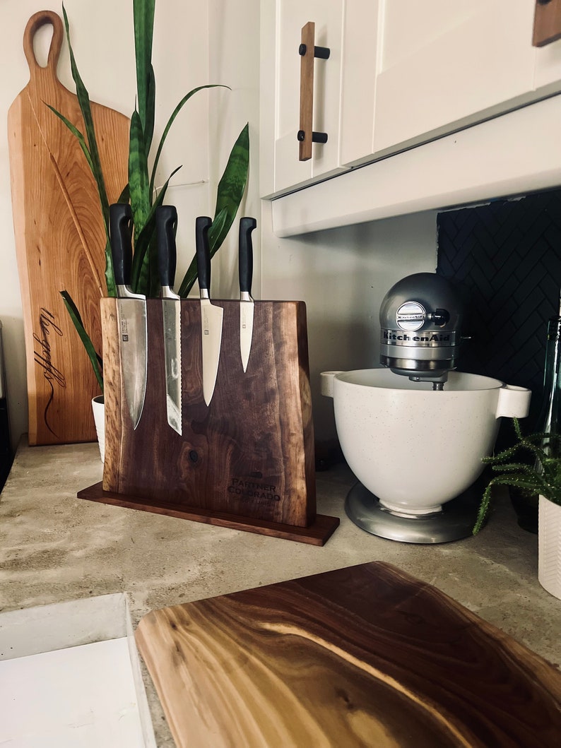 May include: A wooden knife block with a live edge design, holding a set of four kitchen knives. The block is engraved with the text "Palmer Colorado" and "Est. 1982".