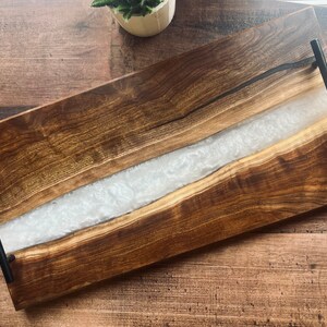 May include: A rectangular wooden serving tray with a white resin inlay and black metal handles.