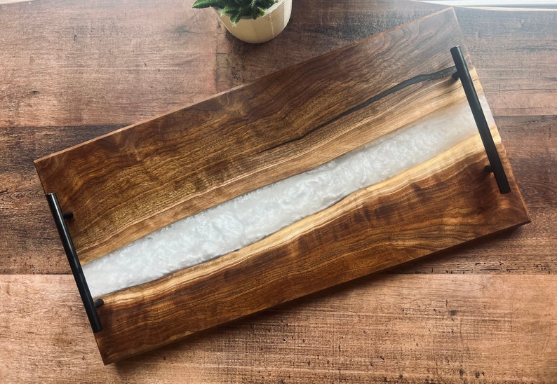 May include: A rectangular wooden serving tray with a white resin inlay and black metal handles.