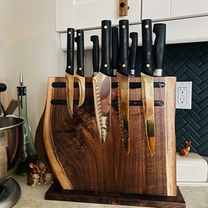 May include: Back of a double-sided knife block made of dark wood with a live edge. The block has a magnetic strip on each side to hold the knives. The knives have black handles and gold blades.