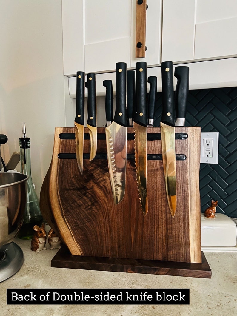 May include: Back of a double-sided knife block made of dark wood with a live edge. The block has a magnetic strip on each side to hold the knives. The knives have black handles and gold blades.
