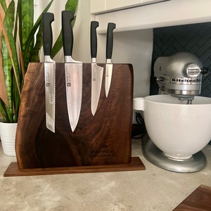 May include: A wooden magnetic knife holder with four silver knives attached. The holder is engraved with the text "Partner Colorado" and "Custom Designs". The holder is sitting on a gray countertop next to a white stand mixer.