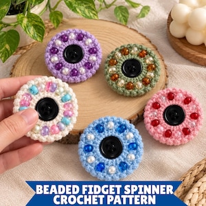 May include: Five circular crochet fidget spinners featuring a central black button surrounded by colorful beads. The spinners are crafted in purple, green, white, blue, and pink yarn with matching and contrasting beads. Text reads: BEADED FIDGET SPINNER CROCHET PATTERN.