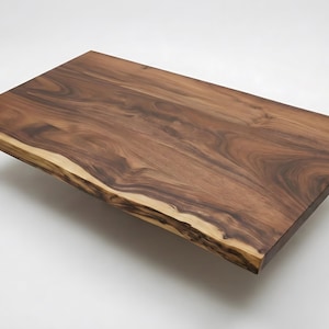 May include: A rectangular, solid wood table top with a natural edge. The wood grain is visible, showcasing a mix of dark brown and lighter tan tones. The table top appears to be floating against a white background.
