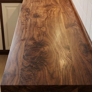 May include: A close-up of a wooden countertop with a rich, dark brown color and intricate wood grain patterns. The countertop is part of a kitchen design, with white cabinets and a tiled backsplash visible.