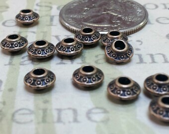 May include: Bronze-colored metal beads with a decorative pattern. The beads have a flat, disc-like shape with a central hole. A US quarter is in the background. These beads are suitable for jewelry making and crafts.