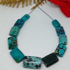 May include: A strand of turquoise beads. The beads are rectangular with a polished finish. The color varies from light to dark turquoise, with brown and black veining. The beads are strung on a thin, dark wire.