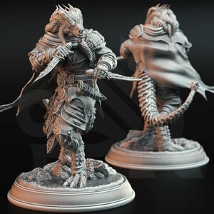 May include: A grey resin miniature figure of a reptilian humanoid warrior standing on a circular base. The figure wears detailed armour, a flowing cape, and holds two daggers. A second view of the same figure from the back is visible behind it.