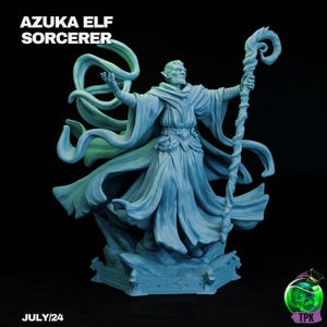 Puede incluir: Figura de Azuka Elf Sorcerer azul claro con túnicas fluidas y un bastón. La figura está sobre una base rocosa. El texto "AZUKA ELF SORCERER" y "JULY/24" son visibles.