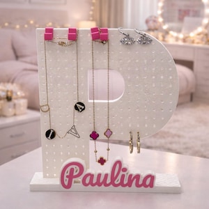 Könnte beinhalten: Ein weißer Schmuck-Organizer in Form des Buchstabens "P" mit rosa Details. Er zeigt Halsketten, Ohrringe und Armbänder. Der Name "Paulina" ist in rosa Schrift auf der Basis geschrieben.