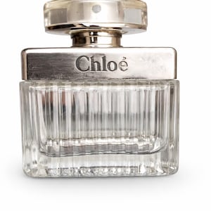 Könnte beinhalten: Ein klarer Glasparfümflakon mit silbernem Verschluss und dem Markennamen "Chloé" auf der Vorderseite. Die Flasche hat eine rechteckige Form mit vertikalen Linien, die in das Glas geätzt sind.
