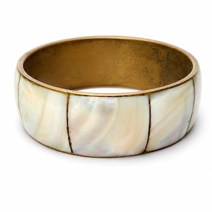 Op de afbeelding: Een brede, goudkleurige metalen armband met een parelmoer inleg. De armband heeft een segmentontwerp met verticale lijnen die de iriserende, crèmekleurige secties scheiden. De binnenkant van de armband is warm goudkleurig.