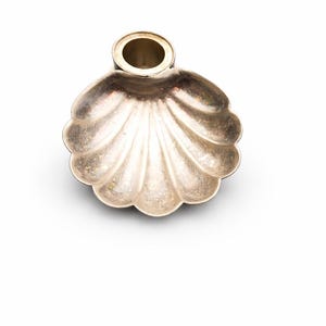 May include: A silver-colored, shell-shaped decorative item with a small, cylindrical opening at the top. The item has a scalloped edge and a metallic sheen, suggesting it is made of metal.