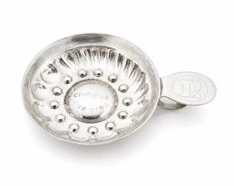 Peut inclure: Un taste-vin en argent avec une poignée. Le taste-vin a une coupe circulaire avec un bord décoratif et un cercle central avec le texte "CIVRIEUX AUX VINS". La poignée porte la lettre "P" gravée.