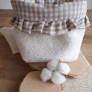 Peut inclure: Un panier blanc et duveteux avec une bordure à carreaux marron et blanc. Le panier repose sur une surface en bois avec des accents de coton, créant une esthétique rustique et chaleureuse. Idéal pour la décoration intérieure ou le rangement.