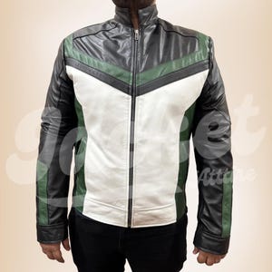 Puede incluir: Chaqueta de cuero negra, blanca y verde, con cremallera. La chaqueta presenta un cuello alzado y un diseño de bloques de color, con detalles de chevron verdes y blancos en el pecho. Las mangas son negras con detalles verdes.
