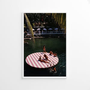 Peut inclure: Tirage encadré d'une photographie vintage montrant une plateforme circulaire rayée rouge et blanche sur un lac. Des personnes sont sur la plateforme et dans l'eau. Des palmiers et des parasols sont en arrière-plan.