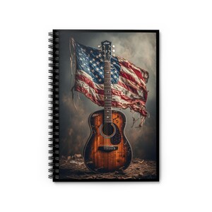 May include: Spiral-bound notebook featuring a distressed acoustic guitar and a tattered American flag. The guitar has a brown finish with visible wear, and the flag displays the stars and stripes. The background has a smoky, textured appearance.