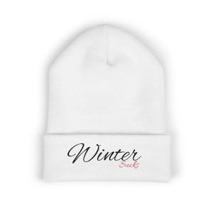 May include: White beanie with the words "Winter Sucks" in black script and red text. The hat is made of a soft, knitted material and is designed to keep the head warm. The beanie is a winter accessory.