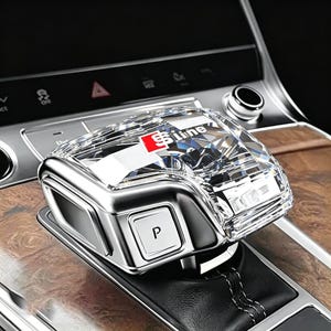 May include: A crystal-style gear shift knob featuring a faceted, transparent top with the red and white S line logo printed on the surface. The base is metallic silver with a square button marked with the letter P, set on a black leather boot.