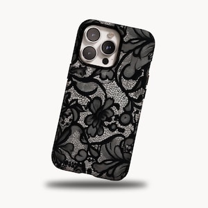 May include: Black and white floral lace phone case. The case features a detailed, intricate lace pattern with a dark background and a glossy finish. The design includes floral and swirling elements, creating a sophisticated look.