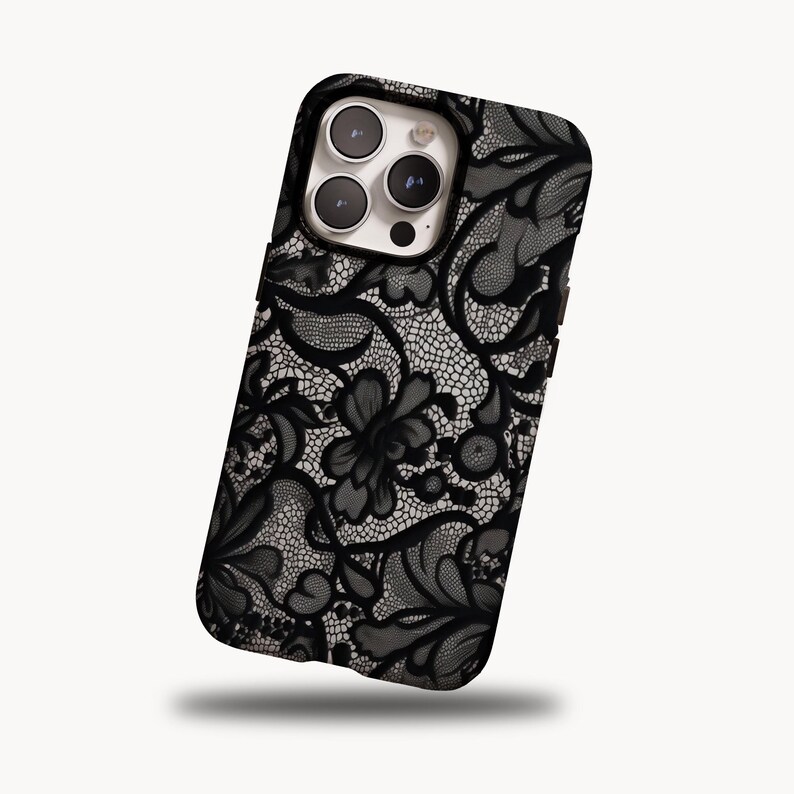 May include: Black and white floral lace phone case. The case features a detailed, intricate lace pattern with a dark background and a glossy finish. The design includes floral and swirling elements, creating a sophisticated look.