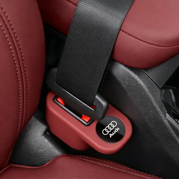 以下が含まれることがあります： 白文字のAudiロゴと4つの重なり合うリングが特徴のマルーン色のシートベルトバックルカバー。このカバーは、ステッチが施されたマルーン色のレザーシートの間に位置する黒いシートベルト機構に取り付けられています。