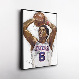 May include: Watercolor-style print of a basketball player in a Sixers jersey, number 6. The player is mid-shot, holding the ball above his head. The artwork has a white background with paint splatters and is framed in black.