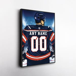 May include: Framed artwork of a hockey player from the back, wearing a navy blue jersey with red and white accents. The jersey displays the number "00" and the text "ANY NAME". The player is wearing a helmet and is on the ice.