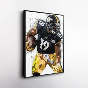 May include: Framed artwork depicting an American football player in a black and gold uniform, number 19, holding a football. The painting has a watercolour effect with white and grey splatters.