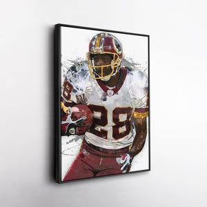 May include: Framed artwork of a football player in a burgundy and gold uniform, number 28. The player is wearing a helmet and holding a football. The artwork has a watercolor effect with paint splatters.