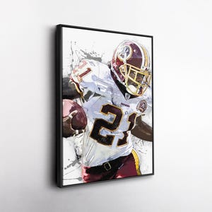 May include: Framed artwork of an American football player in a burgundy and gold helmet and jersey, holding a football. The player's jersey displays the number 21 in large black numerals. The artwork has a watercolor effect with paint splatters.
