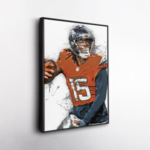 May include: Framed art print of a football player in an orange and blue uniform, number 15, holding a football. The artwork has a watercolor effect with paint splatters, set against a white background. The player is wearing a helmet.