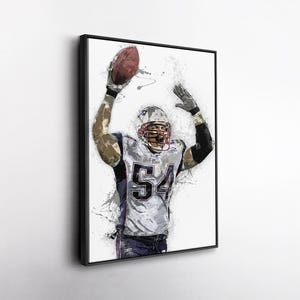 May include: Framed art print of a football player in a white and blue uniform with the number 54. The player is holding a brown football above his head. The artwork has a watercolor effect with paint splatters.