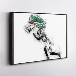 May include: Framed artwork depicting a dynamic football play. A player in green leaps over a player in black and white. The image has a watercolor effect with splashes of color against a white background.