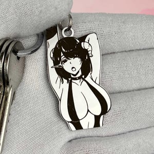 Könnte beinhalten: Ein silberfarbener Schlüsselanhänger mit einer schwarz-weißen Anime-Illustration eines weiblichen Charakters. Der Charakter hat Hörner, einen Halsband und ein gestreiftes Oberteil. Der Schlüsselanhänger ist an einem Schlüsselring mit mehreren Schlüsseln befestigt.