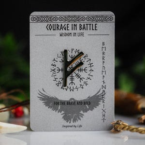 Pode incluir: Alfinete de metal com um símbolo rúnico, apresentado num cartão cinzento com o texto "COURAGE IN BATTLE" e "FOR THE BRAVE AND BOLD". O cartão tem uma borda decorativa e um gráfico de pássaro. O alfinete é escuro com detalhes dourados.