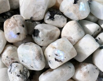 May include: A collection of tumbled moonstone gemstones. The stones are primarily white with iridescent flashes of blue and hints of black and brown. The smooth, rounded stones vary in size and shape, creating a natural, organic aesthetic.